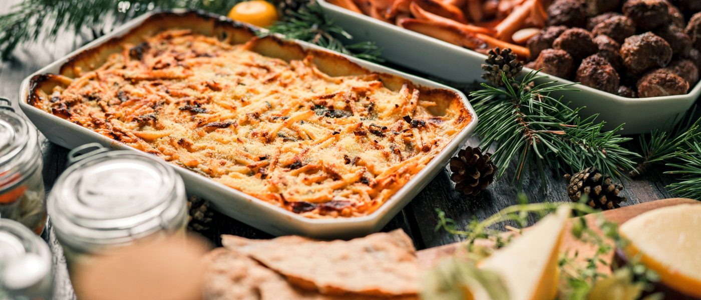 A traditional Swedish Christmas buffet dinner on a dark wooden table, decorated with pine needles, pine cones and candles.